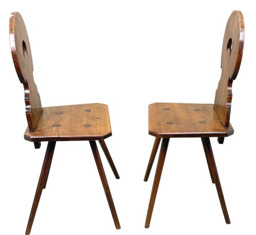fig 1. A pair of mid-19th-century Swiss escabelle chairs crafted from warm brown fruitwood, featuring circular carved backrests with cut-out motifs and four splayed tapered legs.