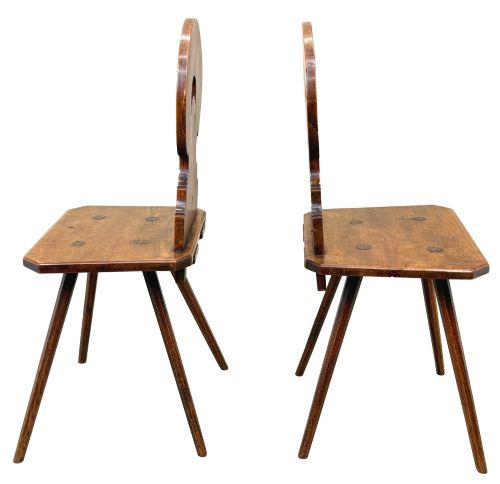 fig 2. A pair of mid-19th-century Swiss escabelle chairs crafted from warm brown fruitwood, featuring circular carved backrests with cut-out motifs and four splayed tapered legs.