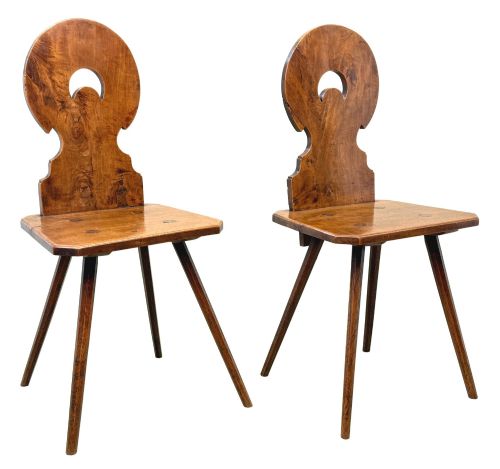 fig 4. A pair of mid-19th-century Swiss escabelle chairs crafted from warm brown fruitwood, featuring circular carved backrests with cut-out motifs and four splayed tapered legs.