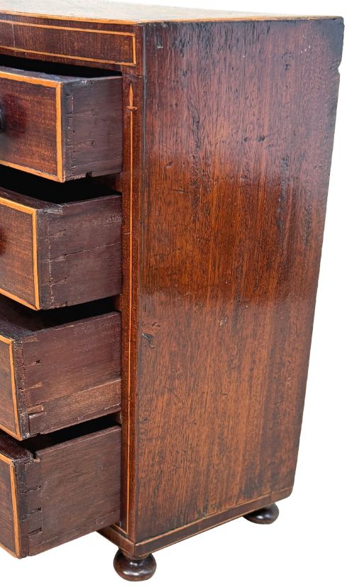 fig 3. An 18th-century Georgian mahogany miniature bowfront chest of drawers featuring boxwood inlay, four graduated drawers with turned wooden knobs, and low bun feet.