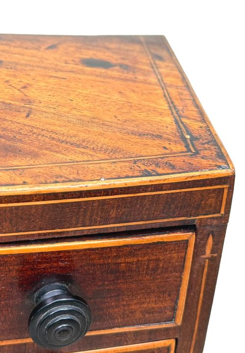 fig 4. An 18th-century Georgian mahogany miniature bowfront chest of drawers featuring boxwood inlay, four graduated drawers with turned wooden knobs, and low bun feet.