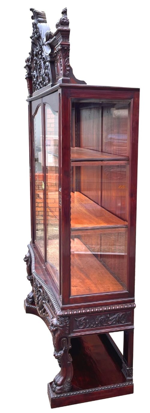 fig 3. A 19th-century dark mahogany display cabinet featuring a carved crest, glazed doors, and lower support with carved lion mask legs.
