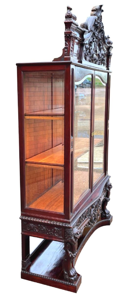 A 19th-century dark mahogany display cabinet featuring a carved crest, glazed doors, and lower support with carved lion mask legs. View X