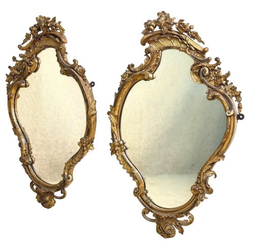 fig 1. A pair of mid-19th-century cartouche-form wall mirrors featuring ornate carved giltwood and gesso frames decorated with scrolling foliage and floral cresting.
