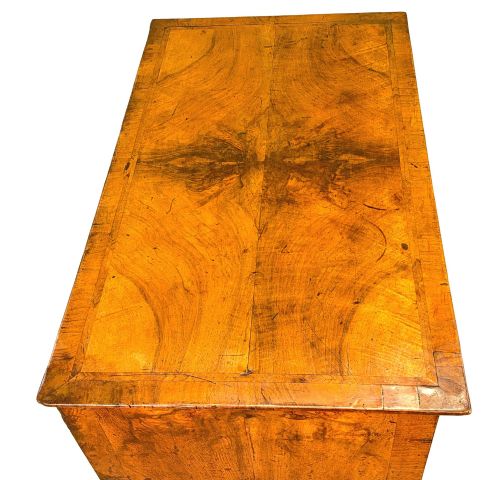 fig 2. An early eighteenth-century Queen Anne walnut chest of drawers featuring two short over three long graduated drawers, brass handles, pierced escutcheons, and turned bun feet.