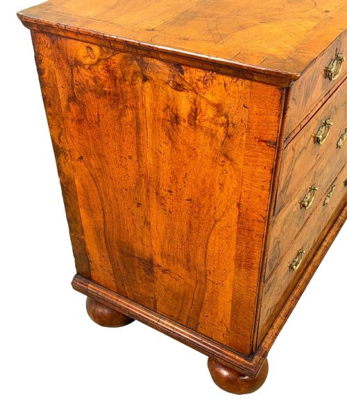 fig 3. An early eighteenth-century Queen Anne walnut chest of drawers featuring two short over three long graduated drawers, brass handles, pierced escutcheons, and turned bun feet.