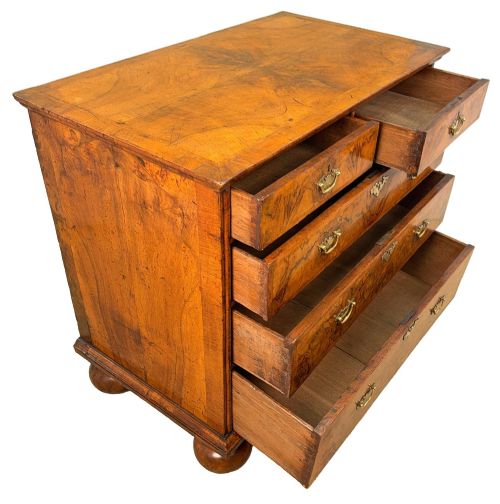 fig 4. An early eighteenth-century Queen Anne walnut chest of drawers featuring two short over three long graduated drawers, brass handles, pierced escutcheons, and turned bun feet.