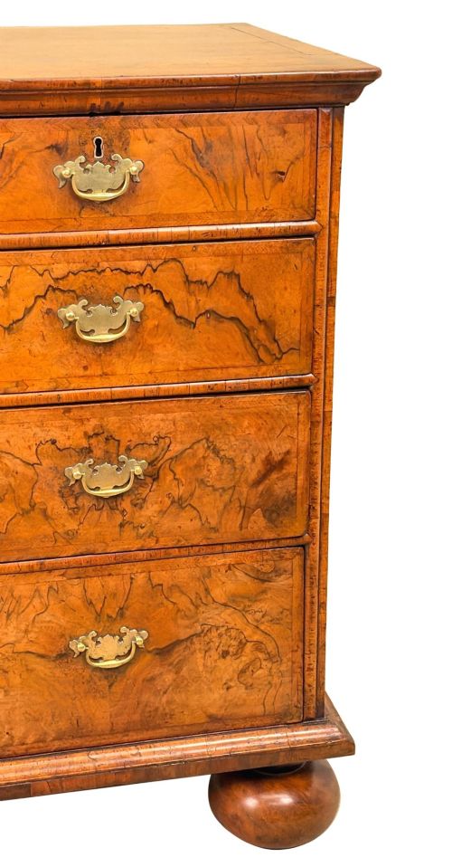 fig 5. An early eighteenth-century Queen Anne walnut chest of drawers featuring two short over three long graduated drawers, brass handles, pierced escutcheons, and turned bun feet.