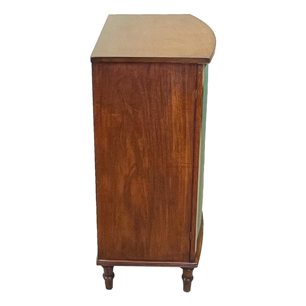 A Regency period bow-fronted mahogany side cabinet featuring two green fabric-panelled doors and turned legs. View III