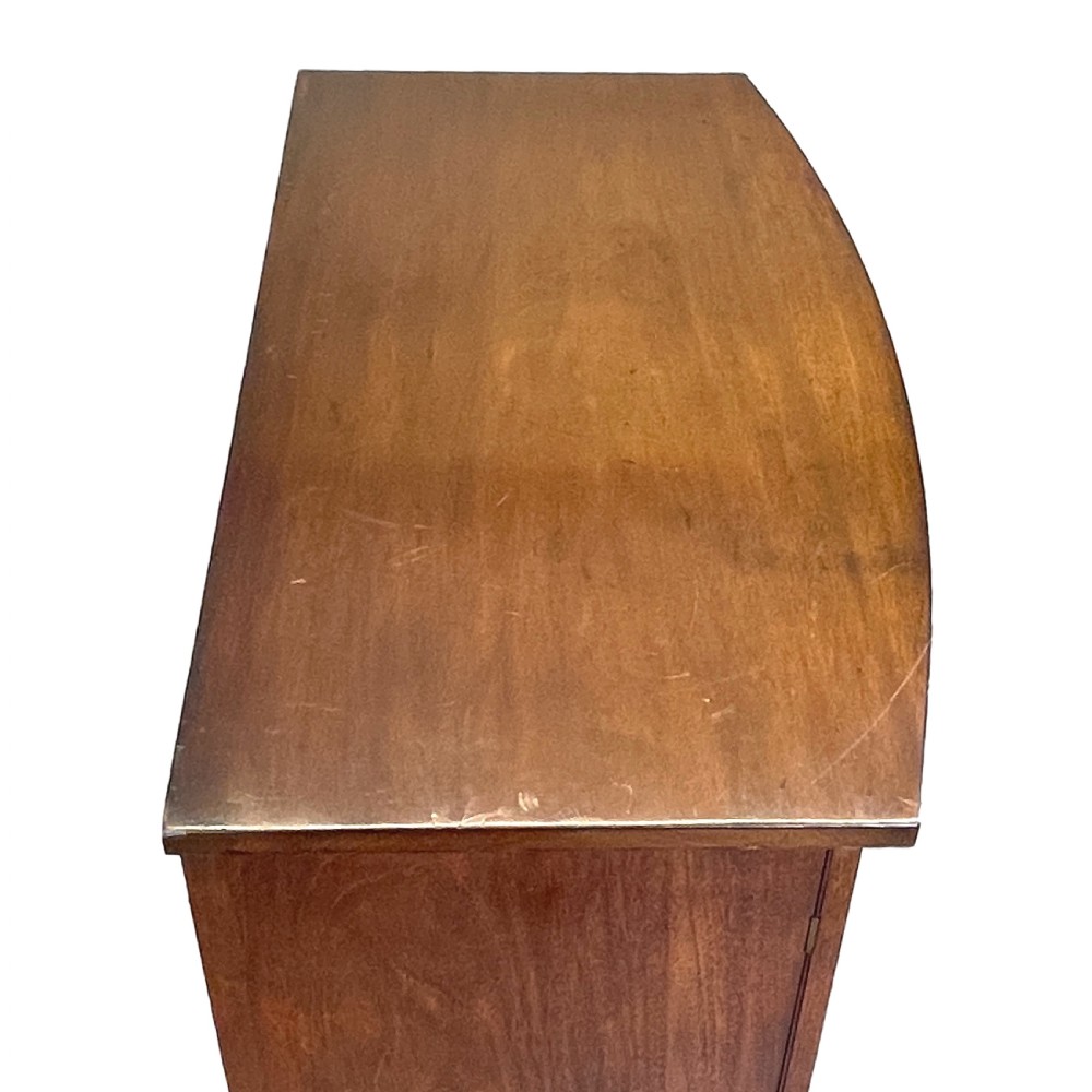 A Regency period bow-fronted mahogany side cabinet featuring two green fabric-panelled doors and turned legs. View IV