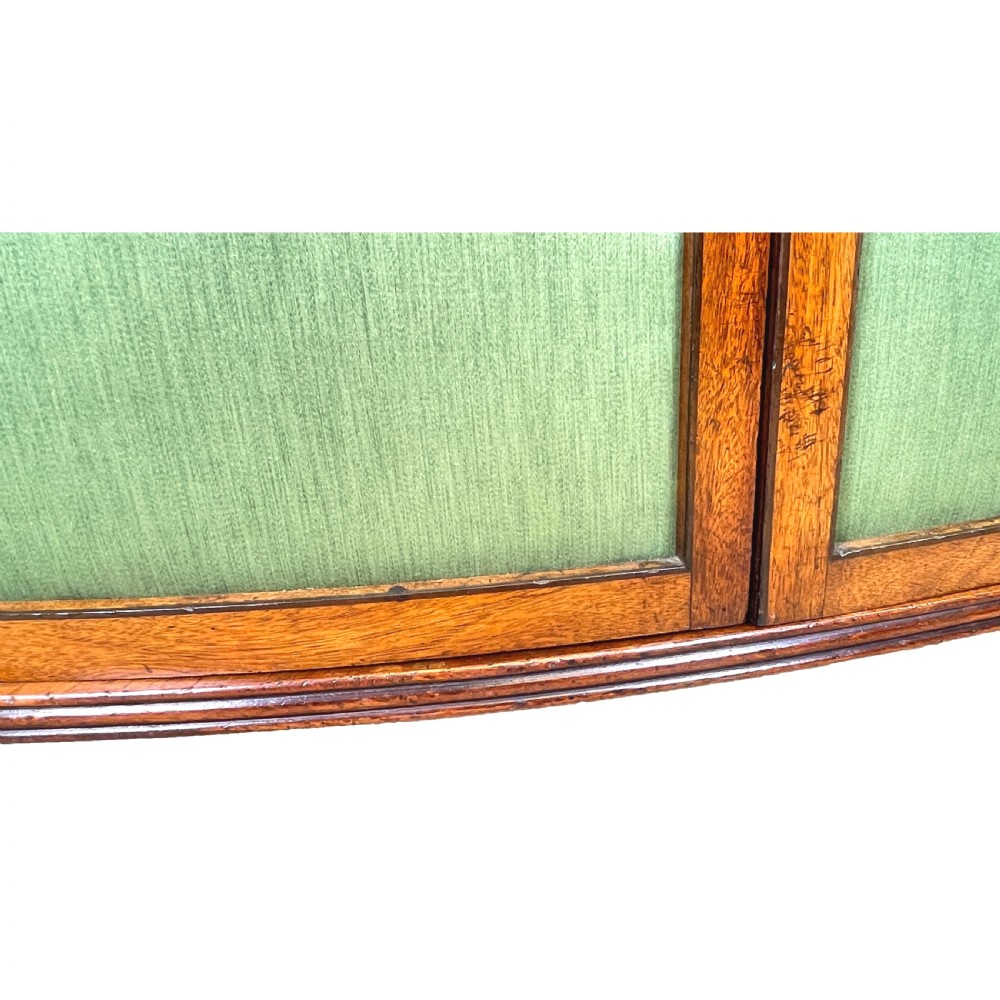 A Regency period bow-fronted mahogany side cabinet featuring two green fabric-panelled doors and turned legs. View VII