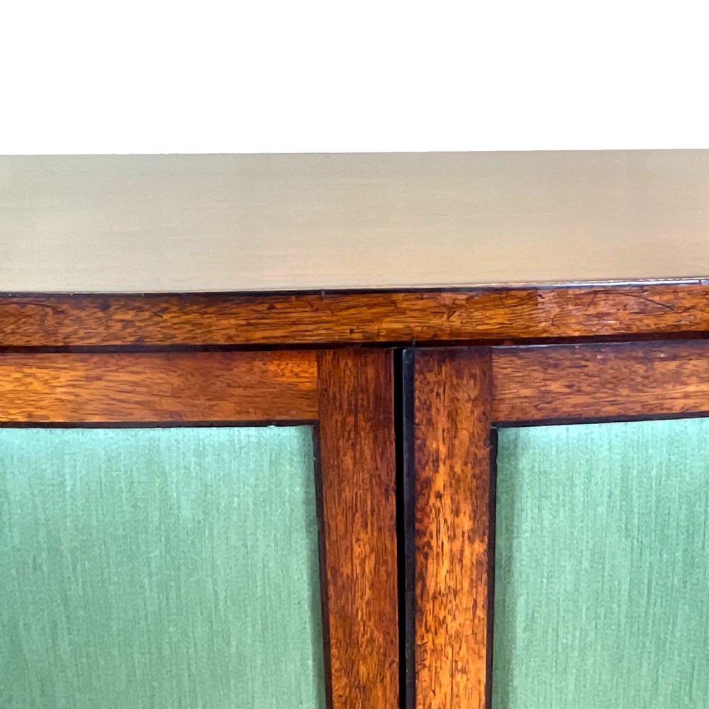 A Regency period bow-fronted mahogany side cabinet featuring two green fabric-panelled doors and turned legs. View IX
