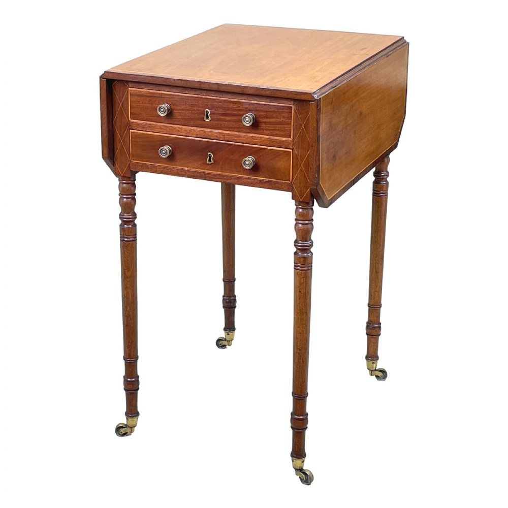 A small Georgian mahogany Pembroke table featuring two drawers with brass handles, fine stringing inlay, two drop leaves, and slender turned legs on brass castors.
