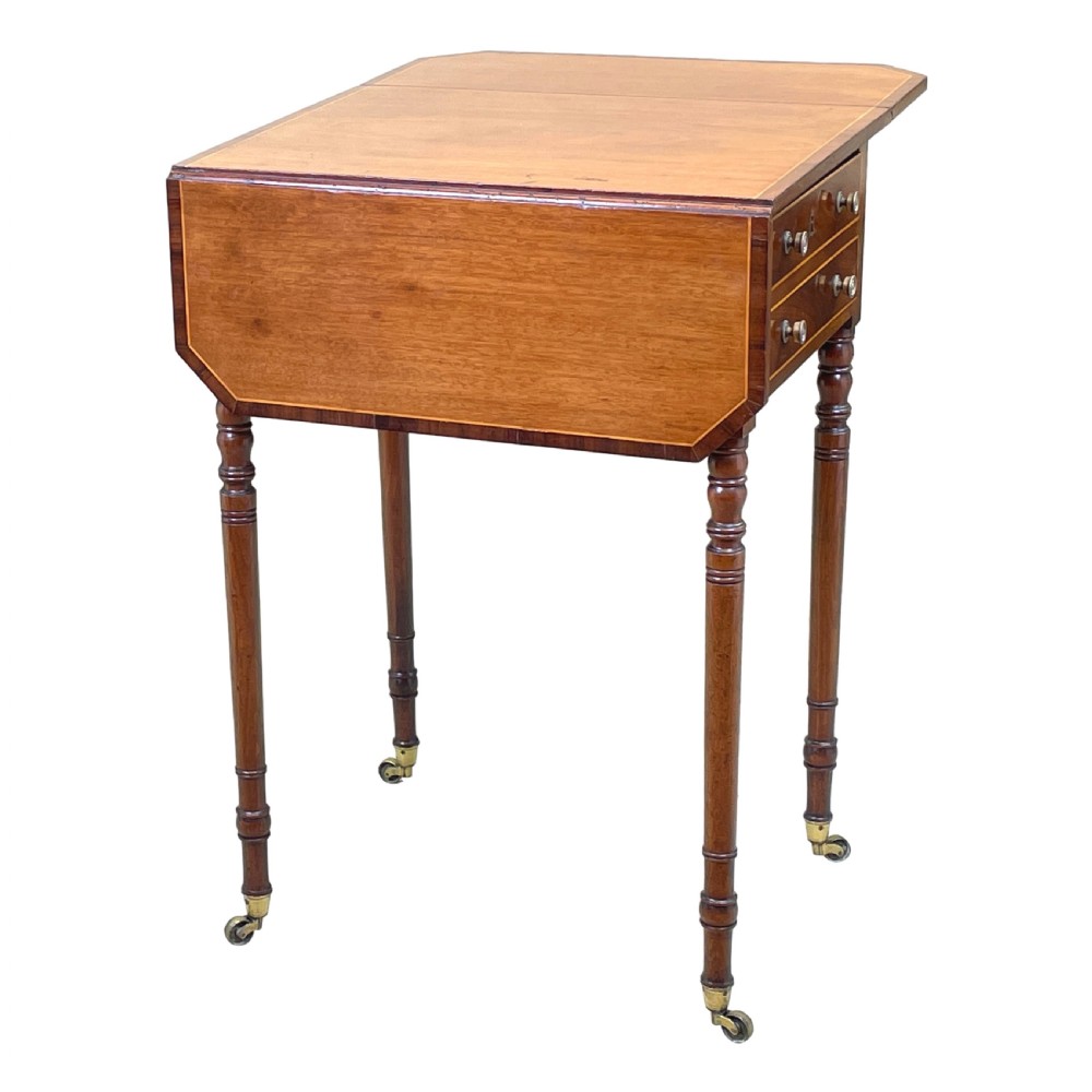 A small Georgian mahogany Pembroke table featuring two drawers with brass handles, fine stringing inlay, two drop leaves, and slender turned legs on brass castors. View V