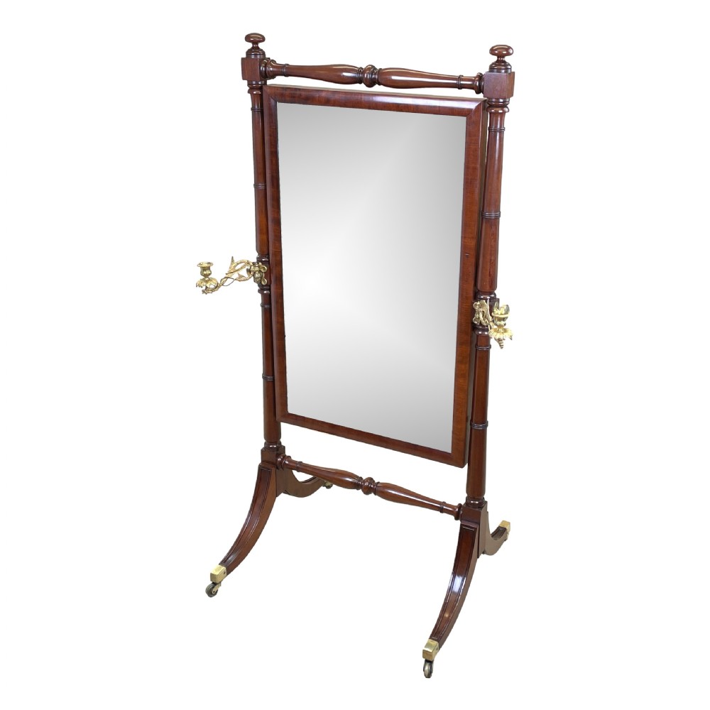 A Georgian mahogany freestanding cheval mirror featuring brass candle sconces, turned upright columns, and splayed legs with brass castors.