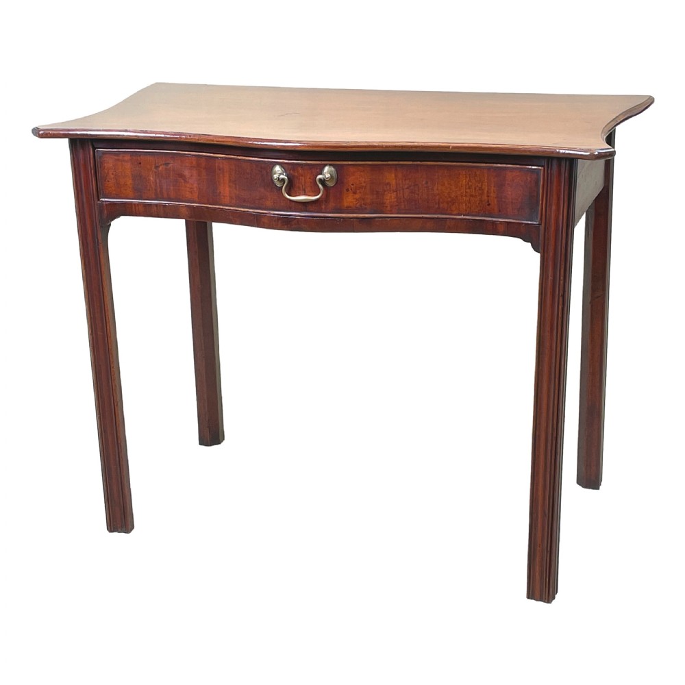 A Georgian mahogany side table featuring a serpentine front, a single drawer with a brass handle, and four straight fluted legs.