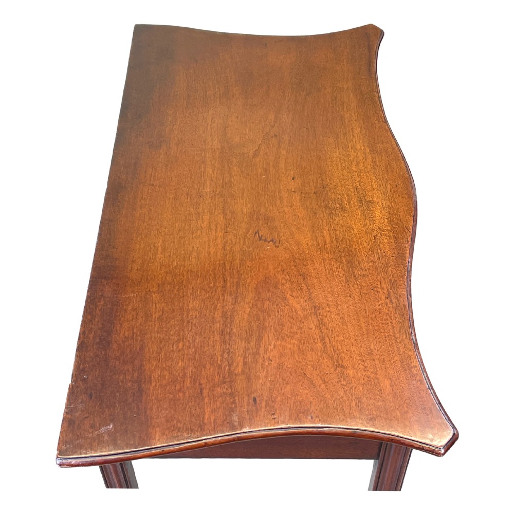 A Georgian mahogany side table featuring a serpentine front, a single drawer with a brass handle, and four straight fluted legs. View II
