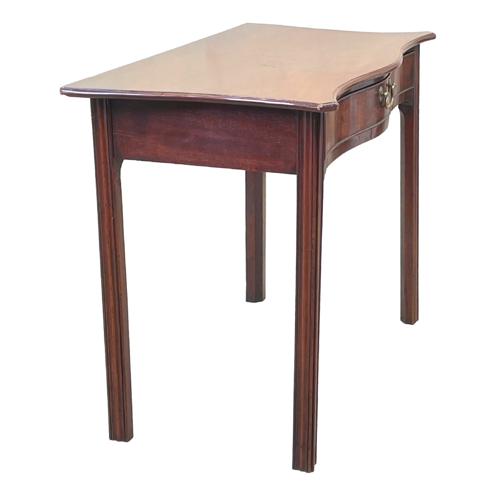 A Georgian mahogany side table featuring a serpentine front, a single drawer with a brass handle, and four straight fluted legs. View VII