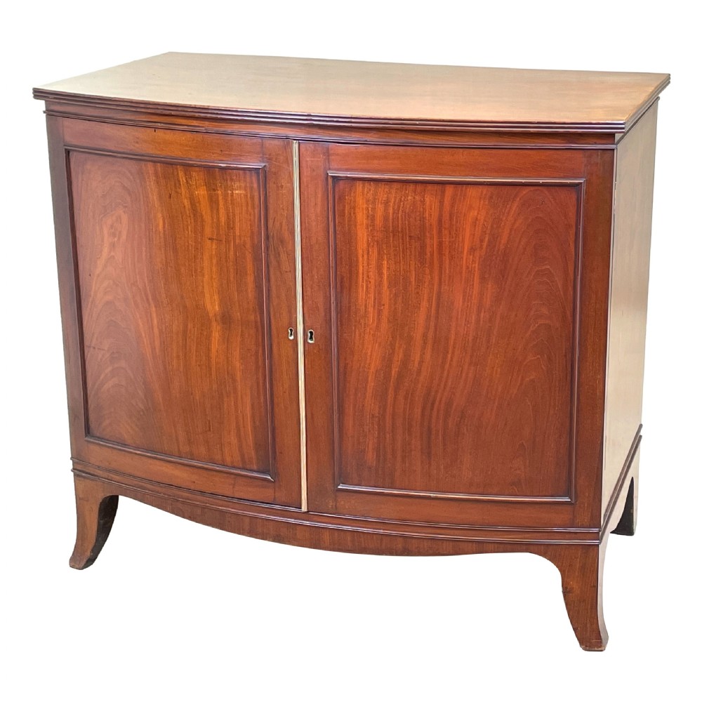 A Georgian bow-front mahogany dwarf cupboard with flame mahogany twin door panels, brass astragal mouldings, and splayed bracket feet.