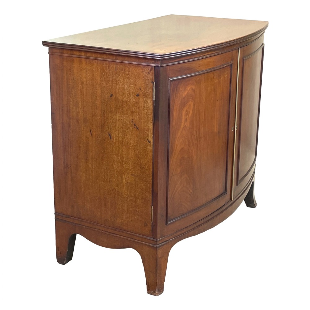 A Georgian bow-front mahogany dwarf cupboard with flame mahogany twin door panels, brass astragal mouldings, and splayed bracket feet. View V