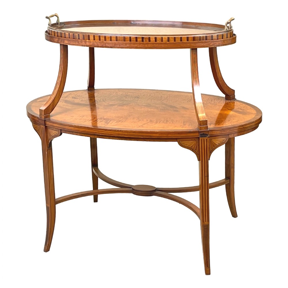 A 19th-century oval satinwood two-tier etagere table featuring geometric stringing inlay, a removable brass-handled upper tray, and outswept legs joined by an X-stretcher.