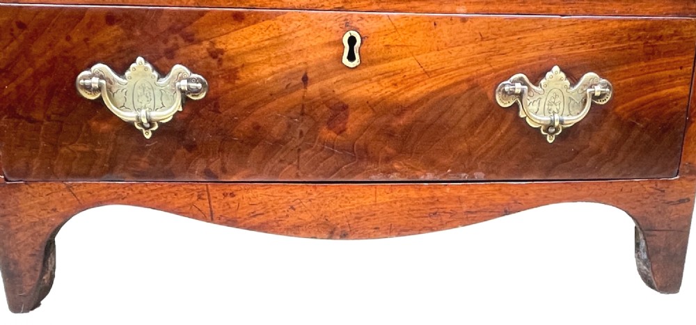 A Georgian mahogany miniature chest of drawers featuring four graduated drawers with ornate brass swan-neck handles and shaped bracket feet. View V