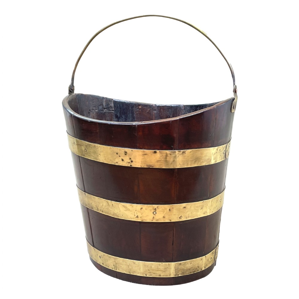 An 18th-century stave-constructed mahogany bucket encircled by three horizontal brass bands with an arched brass swing handle.