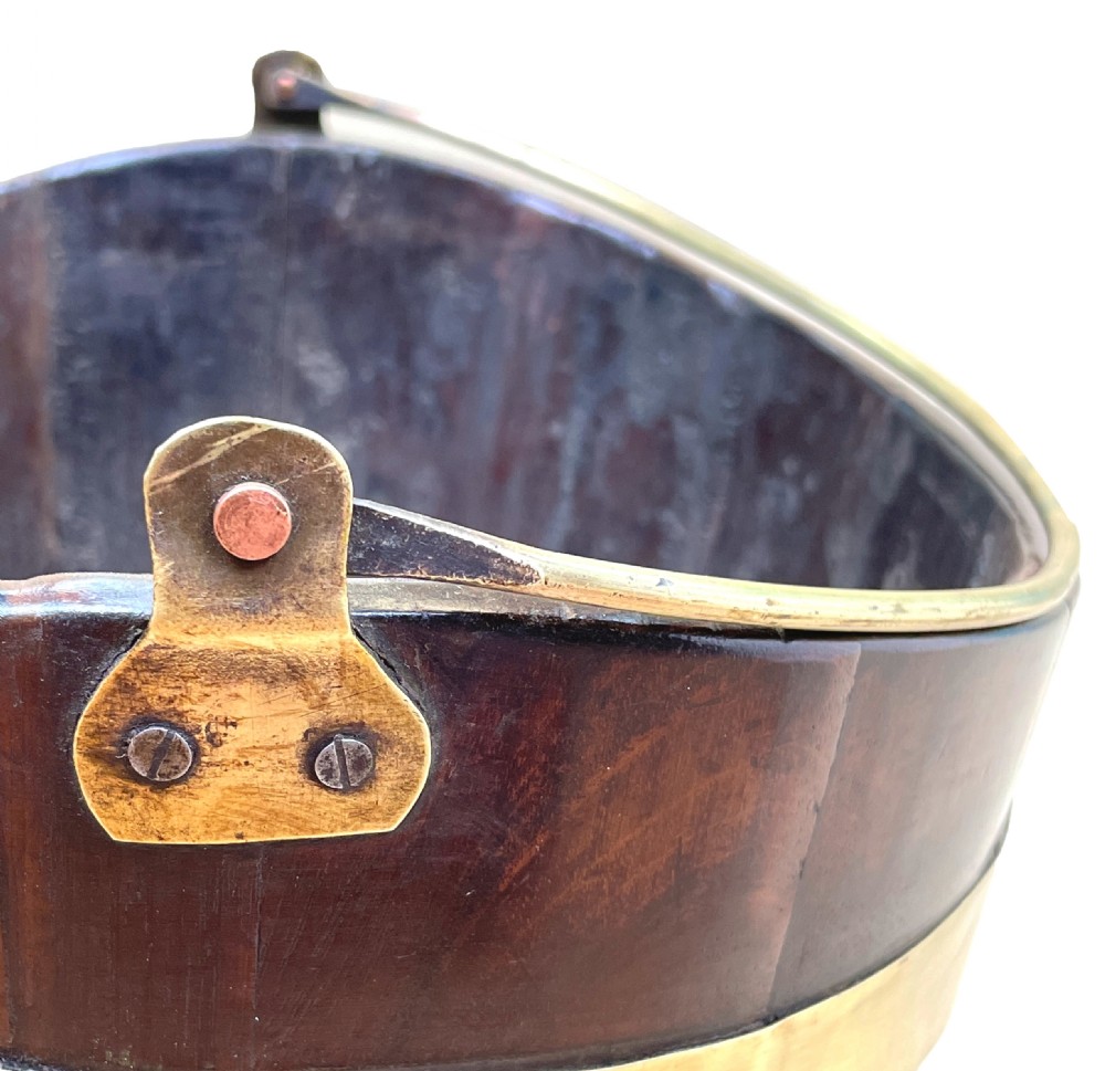 An 18th-century stave-constructed mahogany bucket encircled by three horizontal brass bands with an arched brass swing handle. View V