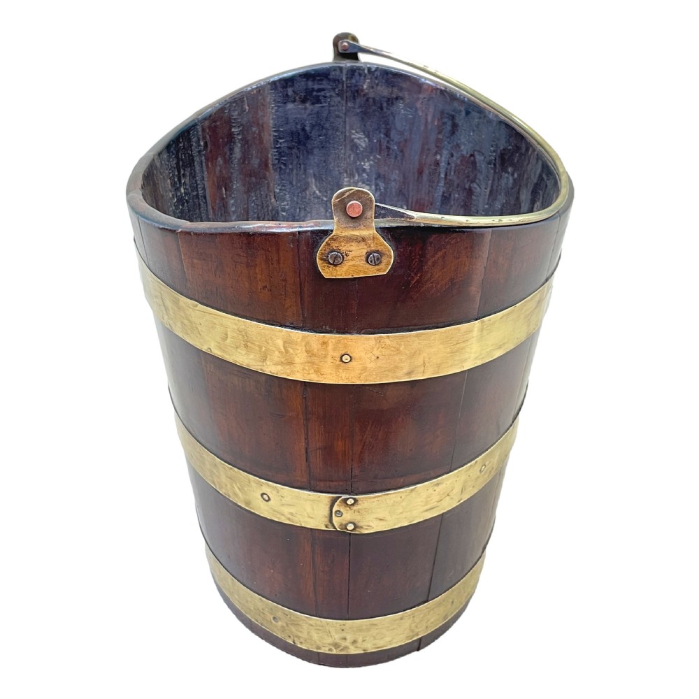 An 18th-century stave-constructed mahogany bucket encircled by three horizontal brass bands with an arched brass swing handle. View VI