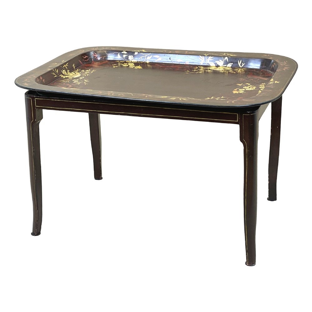 A nineteenth-century dark lacquered papier-mache tray with gold floral decoration resting on a fitted dark wood stand with slender tapered legs.