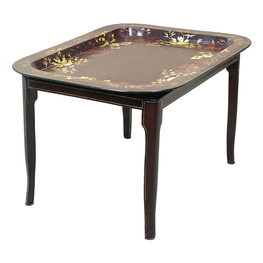 A nineteenth-century dark lacquered papier-mache tray with gold floral decoration resting on a fitted dark wood stand with slender tapered legs. View II