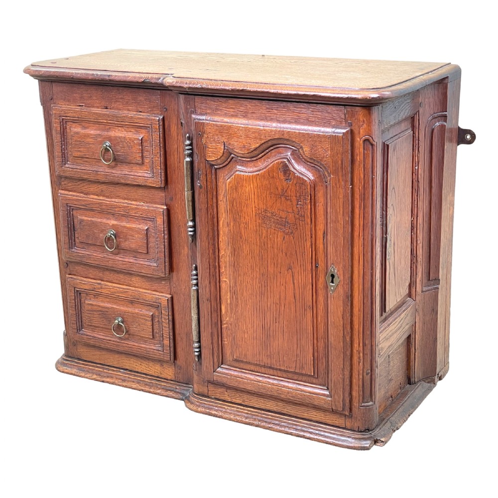 A French Provincial warm oak wall cupboard featuring three stacked drawers on the left and a single panelled door with an arched frame on the right.