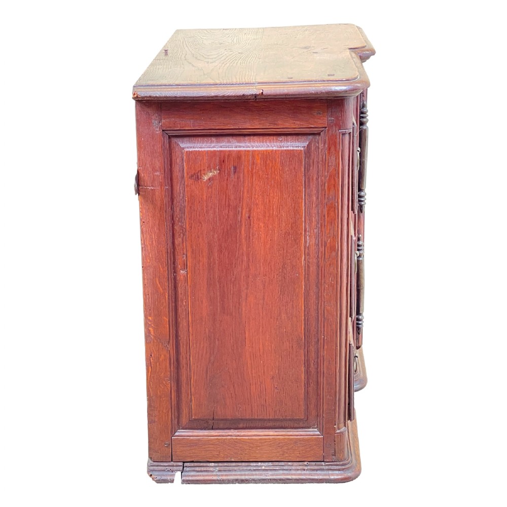 A French Provincial warm oak wall cupboard featuring three stacked drawers on the left and a single panelled door with an arched frame on the right. View II