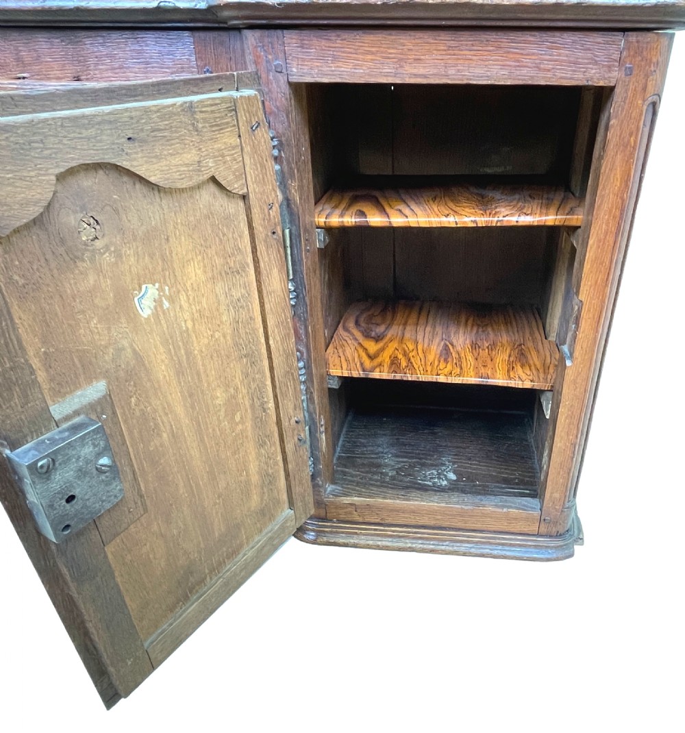 A French Provincial warm oak wall cupboard featuring three stacked drawers on the left and a single panelled door with an arched frame on the right. View VI