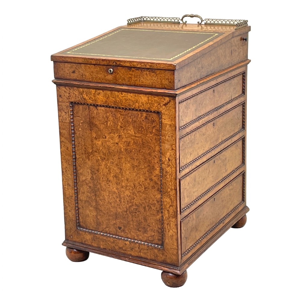 A Regency period burr elm Davenport desk featuring a sloped leather writing surface, a brass gallery railing, side drawers, bead moulding, and turned bun feet.