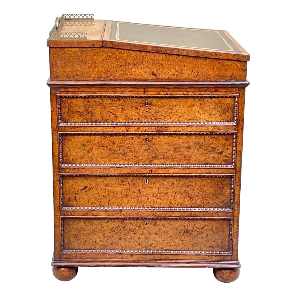 A Regency period burr elm Davenport desk featuring a sloped leather writing surface, a brass gallery railing, side drawers, bead moulding, and turned bun feet. View II