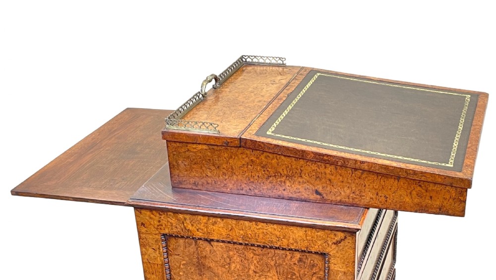 A Regency period burr elm Davenport desk featuring a sloped leather writing surface, a brass gallery railing, side drawers, bead moulding, and turned bun feet. View VI