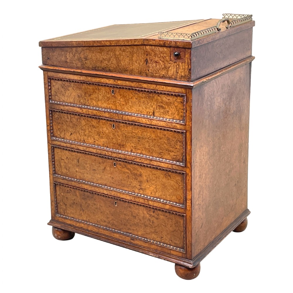 A Regency period burr elm Davenport desk featuring a sloped leather writing surface, a brass gallery railing, side drawers, bead moulding, and turned bun feet. View IX