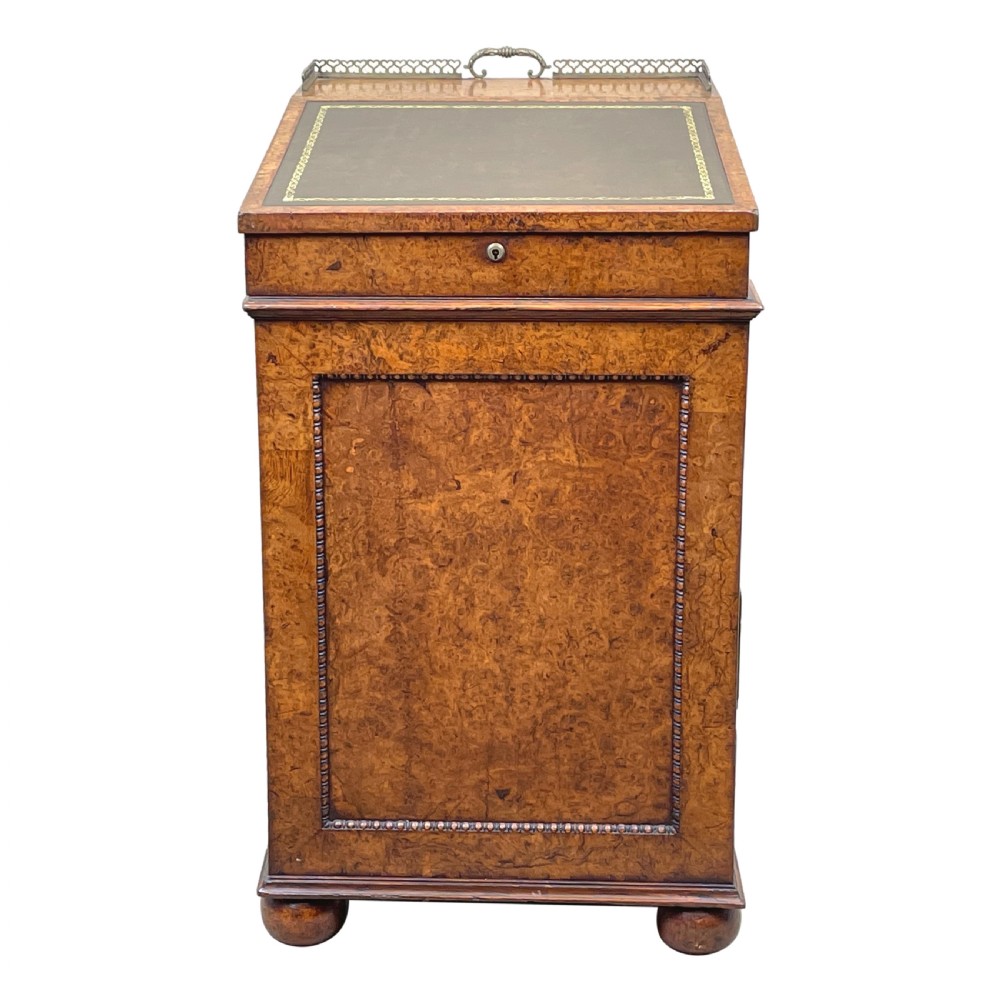 A Regency period burr elm Davenport desk featuring a sloped leather writing surface, a brass gallery railing, side drawers, bead moulding, and turned bun feet. View XI