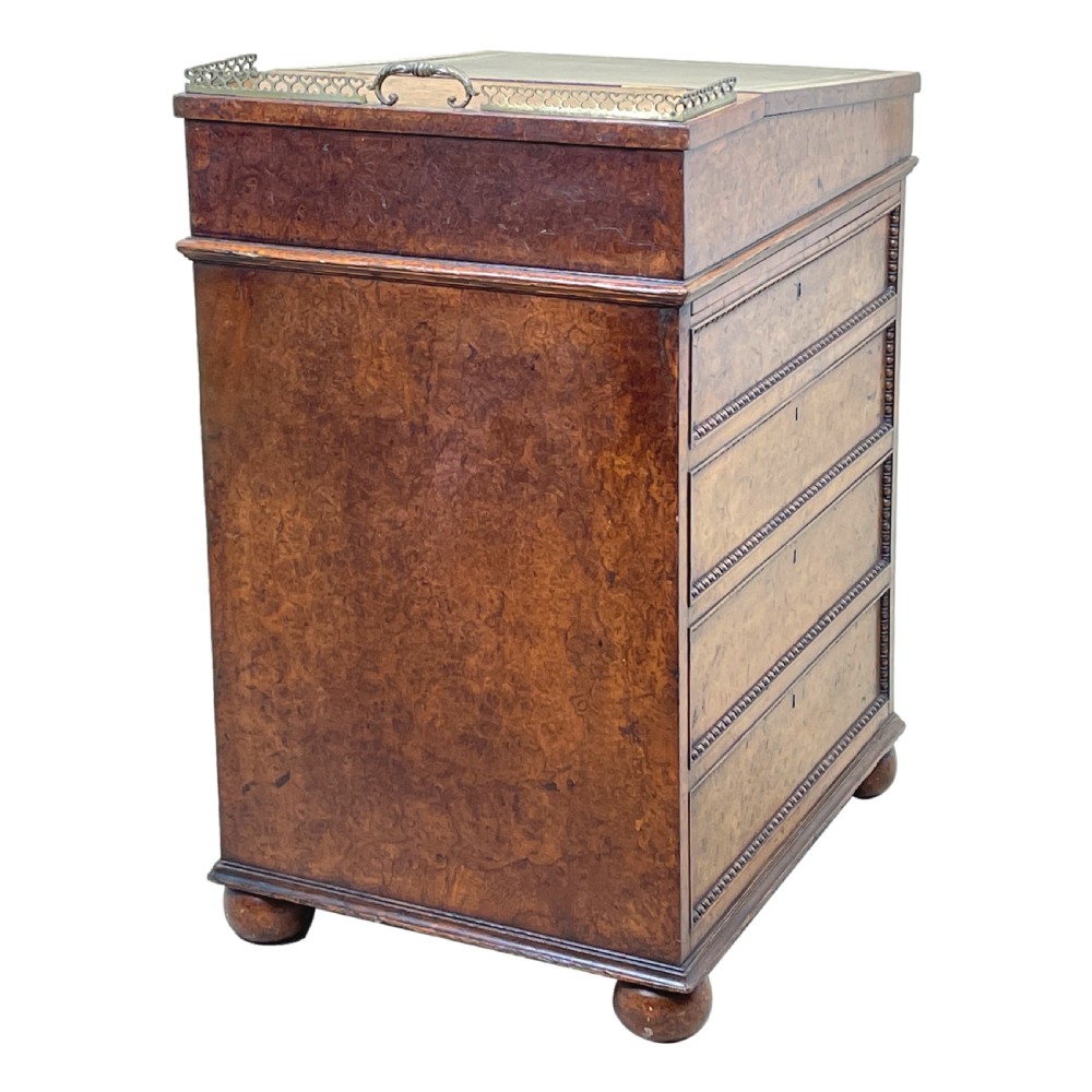 A Regency period burr elm Davenport desk featuring a sloped leather writing surface, a brass gallery railing, side drawers, bead moulding, and turned bun feet. View XIV