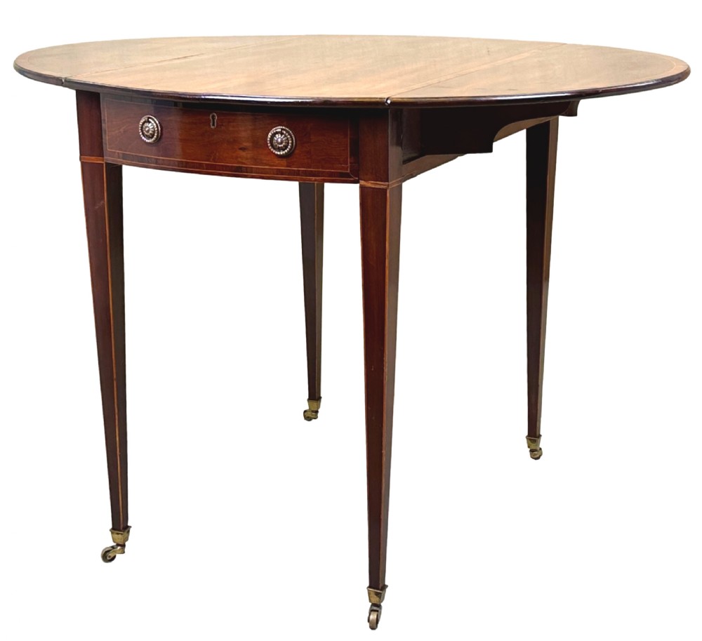 An 18th-century mahogany oval Pembroke table with drop leaves, a single front drawer with brass pull handles, boxwood stringing, square tapered legs, and brass castors.