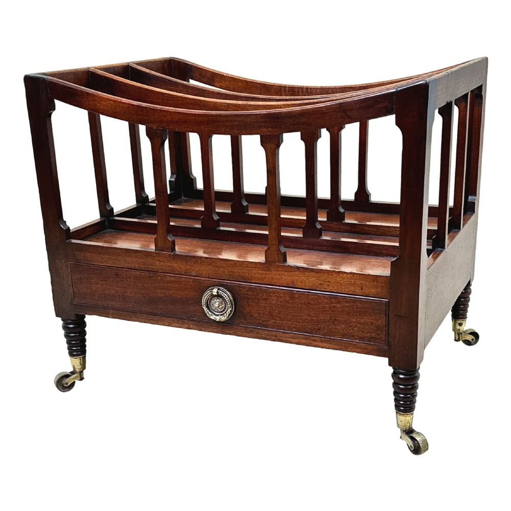 An antique Regency mahogany boat-shaped Canterbury with slatted dividers above a lower drawer on turned legs with brass castors.