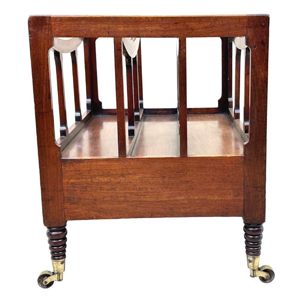 An antique Regency mahogany boat-shaped Canterbury with slatted dividers above a lower drawer on turned legs with brass castors. View II
