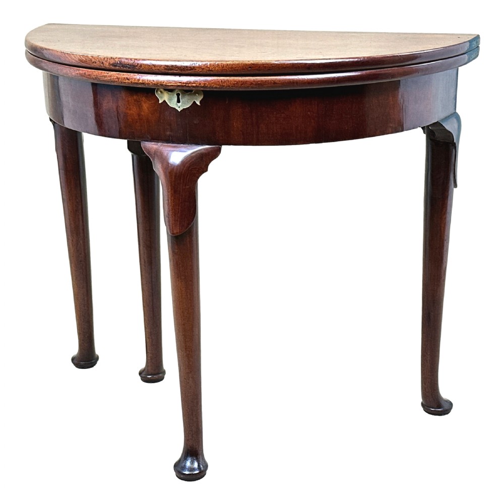 An early Georgian mahogany demilune tea table featuring a fold-over top, a brass escutcheon, and tapered legs ending in pad feet.