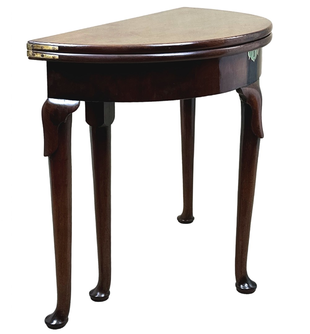 An early Georgian mahogany demilune tea table featuring a fold-over top, a brass escutcheon, and tapered legs ending in pad feet. View IV
