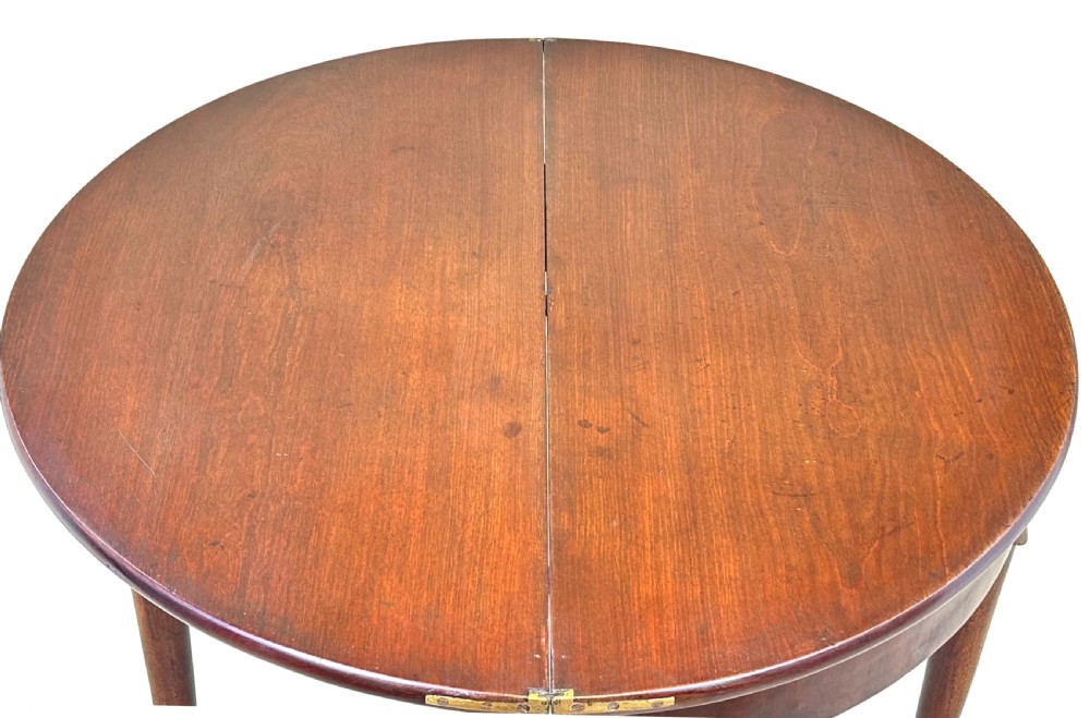 An early Georgian mahogany demilune tea table featuring a fold-over top, a brass escutcheon, and tapered legs ending in pad feet. View XIV