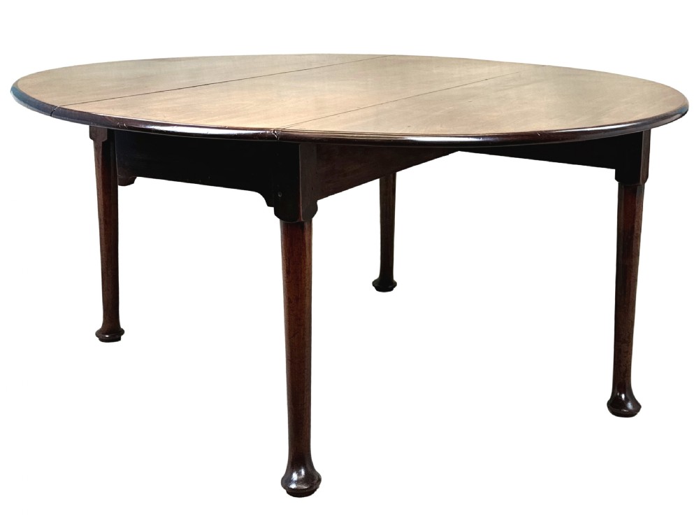 A Georgian dark mahogany drop-leaf dining table with an oval top and tapered legs featuring pad feet.