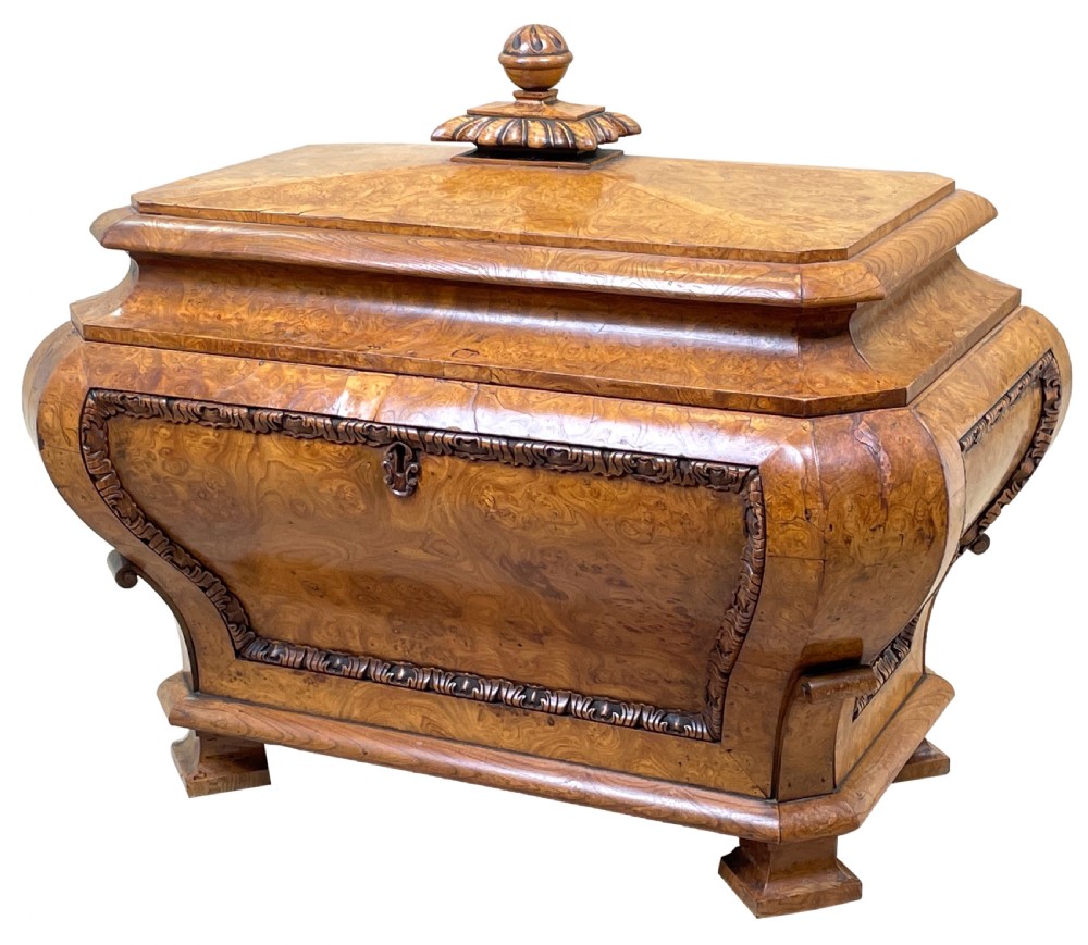 An antique sarcophagus-shaped burr elm cellarette with a carved top finial, gadrooned moulding, and a brass keyhole escutcheon.