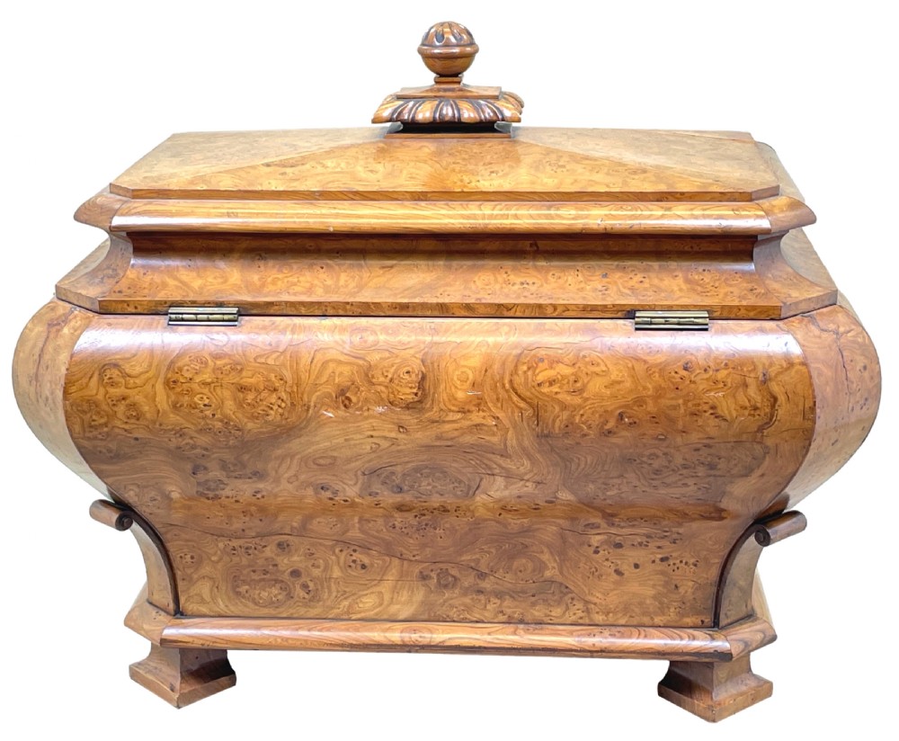 An antique sarcophagus-shaped burr elm cellarette with a carved top finial, gadrooned moulding, and a brass keyhole escutcheon. View VII