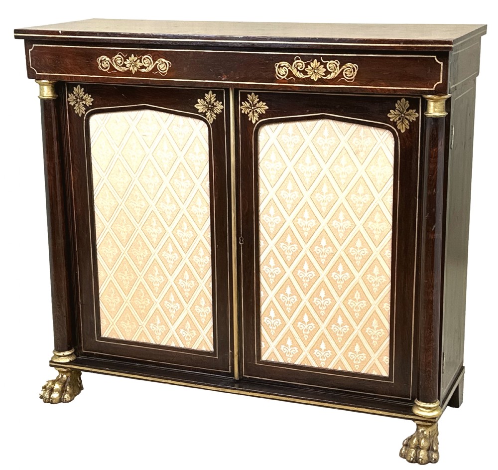 A Regency simulated rosewood side cabinet with gilded floral details, fabric door inserts, side columns, and gilded lion paw feet.